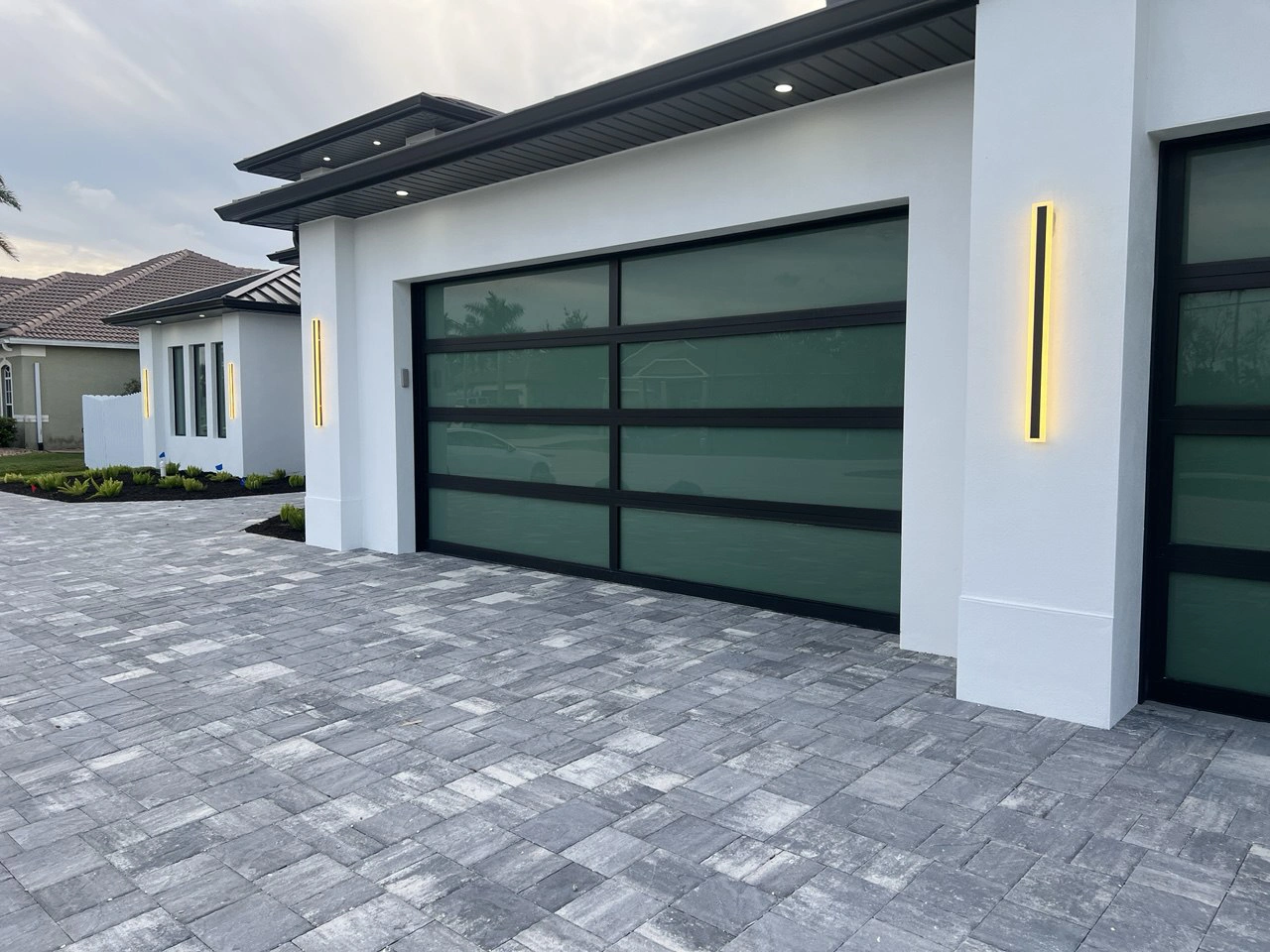 AA Impact impact glass garage doors installed on a modern South Florida luxury home at dusk.